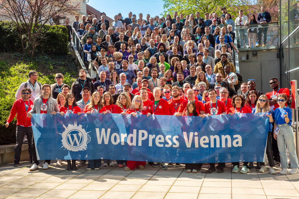 Group picture of attendees of WordCamp Vienna 2026 standing on a big staircase, the front row holding a big 'WordPress Vienna' banner.